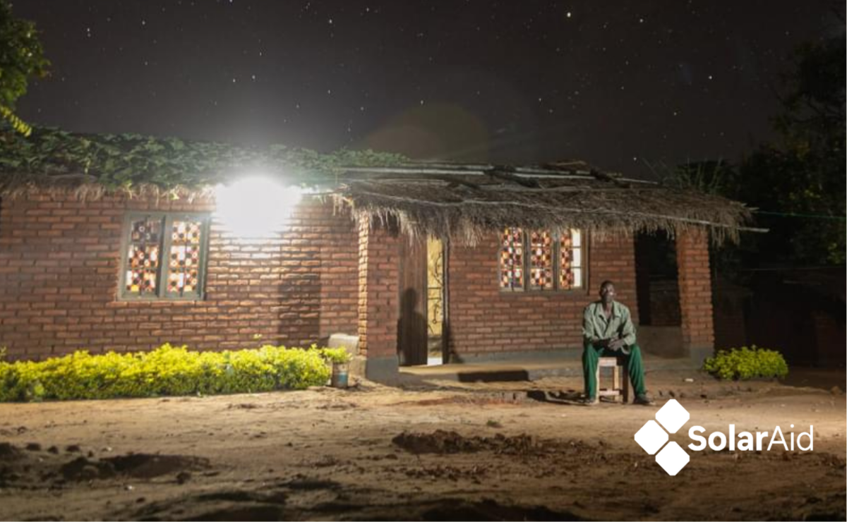 A man sits outside a rural house with a light on in Malawi